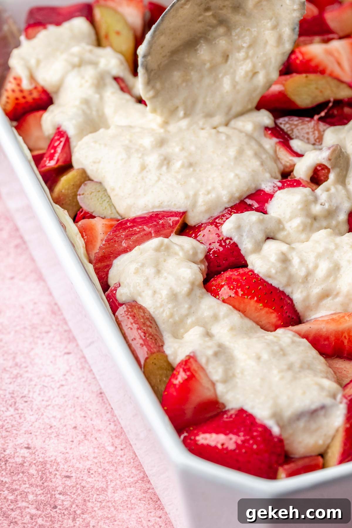 Strawberry Rhubarb Cobbler Recipe: Classic Summer Dessert 7 A spoon pours batter on top of strawberries and rhubarb in a casserole dish.