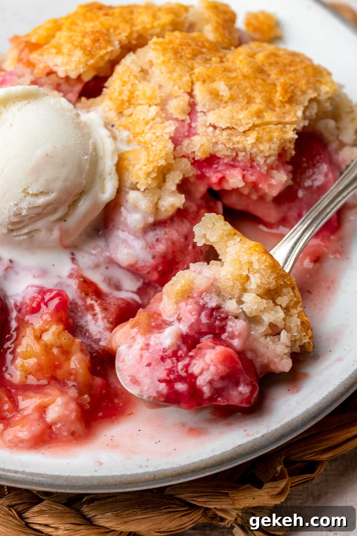 Strawberry Rhubarb Cobbler Recipe: Classic Summer Dessert 10 Strawberry rhubarb cobbler on a plate with a scoop of vanilla ice cream on top. A spoon holds a scoop.