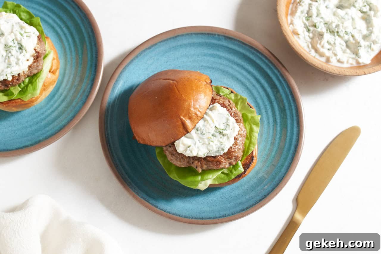 Juicy Ground Lamb Burgers with Creamy Feta Sauce 2 A lamb burger topped with feta yogurt sauce with a bun on a blue plate, a bowl of sauce is in the upper right corner.