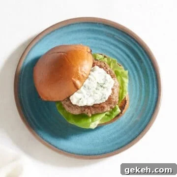 Juicy Ground Lamb Burgers with Creamy Feta Sauce 8 A lamb burger topped with feta yogurt sauce with a bun on a blue plate.