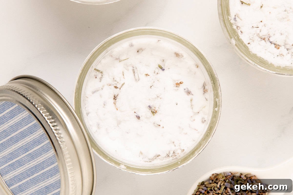 DIY Baking Soda Air Freshener with Natural Scents 6 mason jars of homemade air freshener with a bottle of lavender essential oil and a spoonful of lavender buds next to it