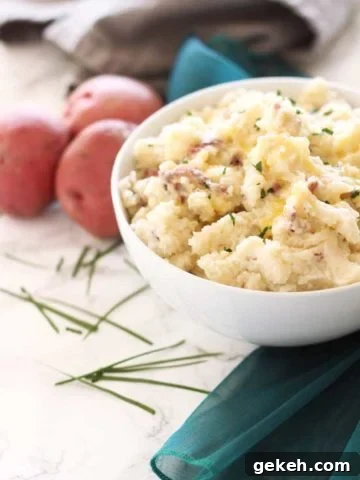 White bowl containing homemade mashed potatoes topped with chives.