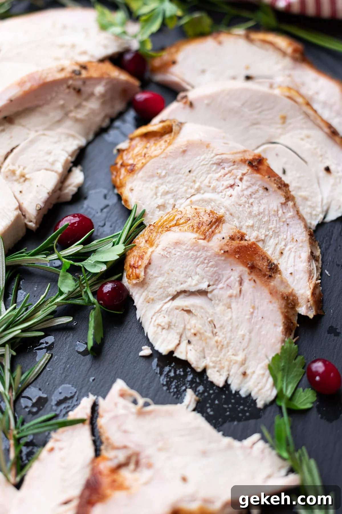 Sliced turkey breast on a plate, cranberries and rosemary on table.