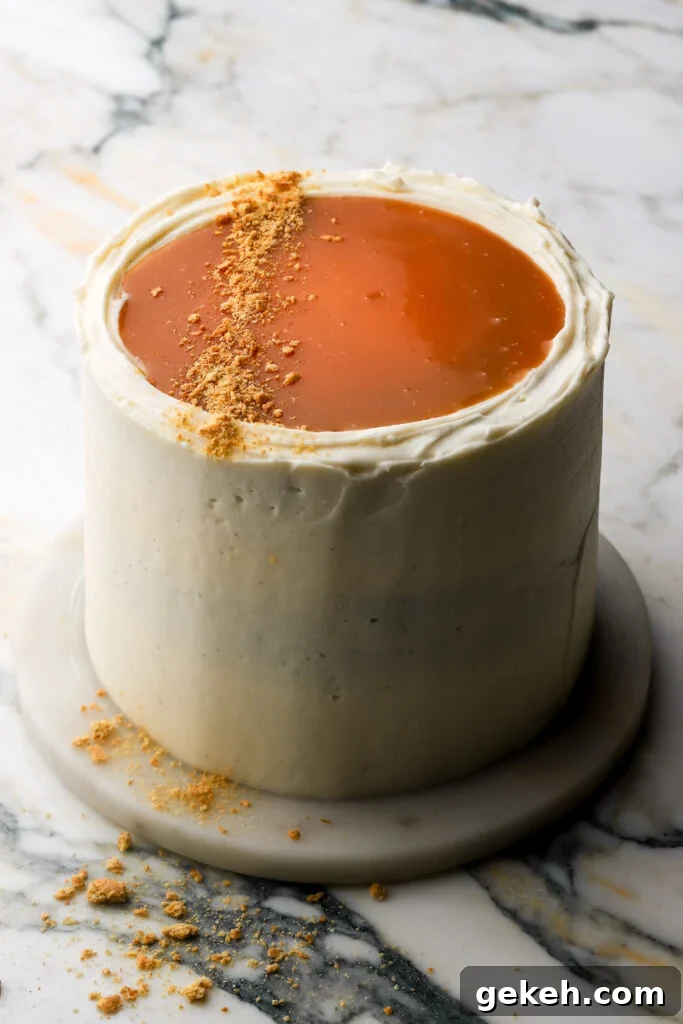 pumpkin cake fully frosted with cream cheese frosting and topped with salted caramel sauce and crushed graham crackers