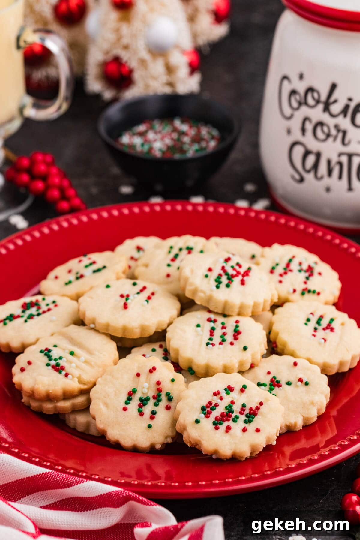 Christmas shortbread cookies with red, green, and white sprinkles on a red plate, next to a 'Cookies for Santa' jar and festive holiday decor.
