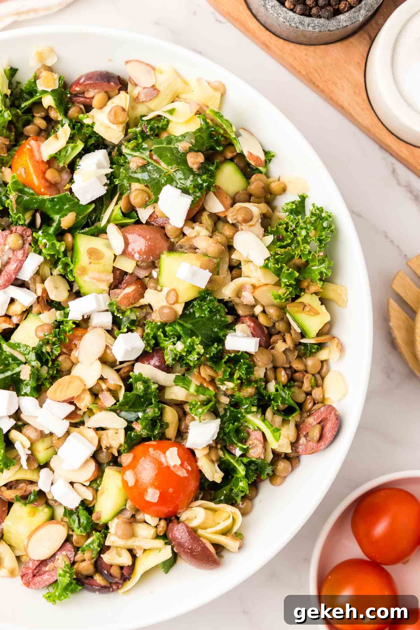 Protein-Packed Lentil and Kale Salad with Lemon Tahini Dressing 2 Overhead view into a large bowl of a kale salad with lentils, artichoke hearts, cucumber, feta, tomato and olives.