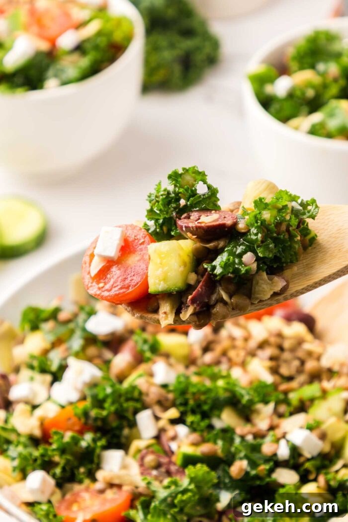 Protein-Packed Lentil and Kale Salad with Lemon Tahini Dressing 8 A wooden spoon with a few piece of kale, cucumber, olives and tomato on it held over a bowl of kale lentil salad.