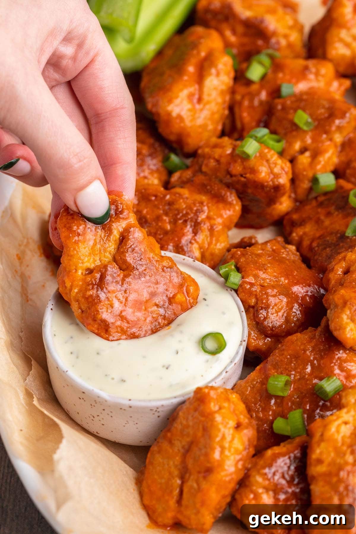 Buffalo-Style Seitan Wings with Spicy Vegan Sauce 4 A white woman's hand holding a buffalo sauced seitan wing as she dips it into a small bowl of ranch dressing.