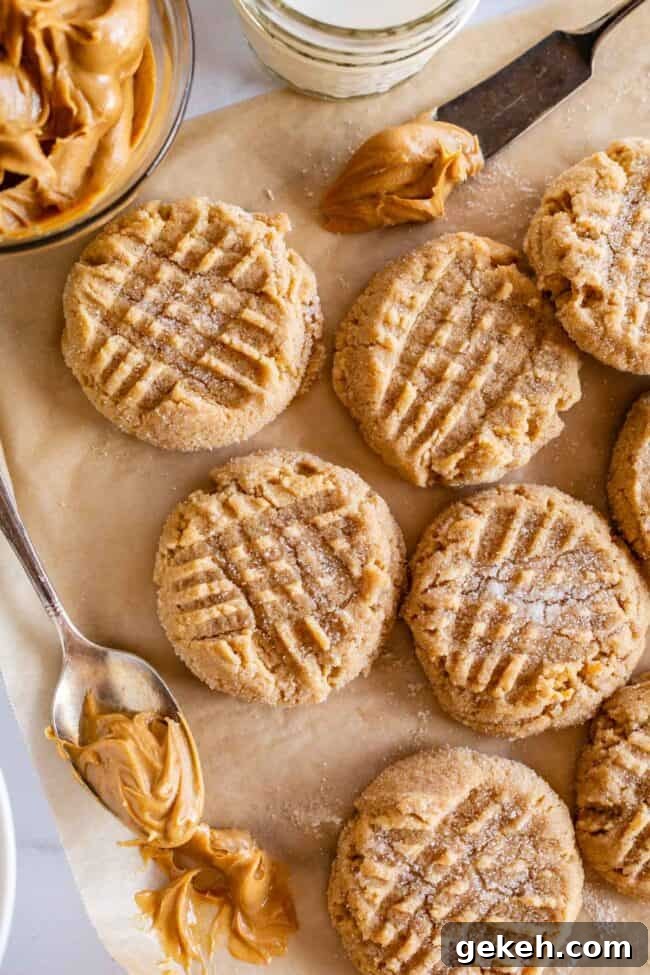 Chewy Peanut Butter Cookie Recipe That Melts in Your Mouth 13 peanut butter cookies on a sheet of brown parchment paper with a spoonful of peanut butter.