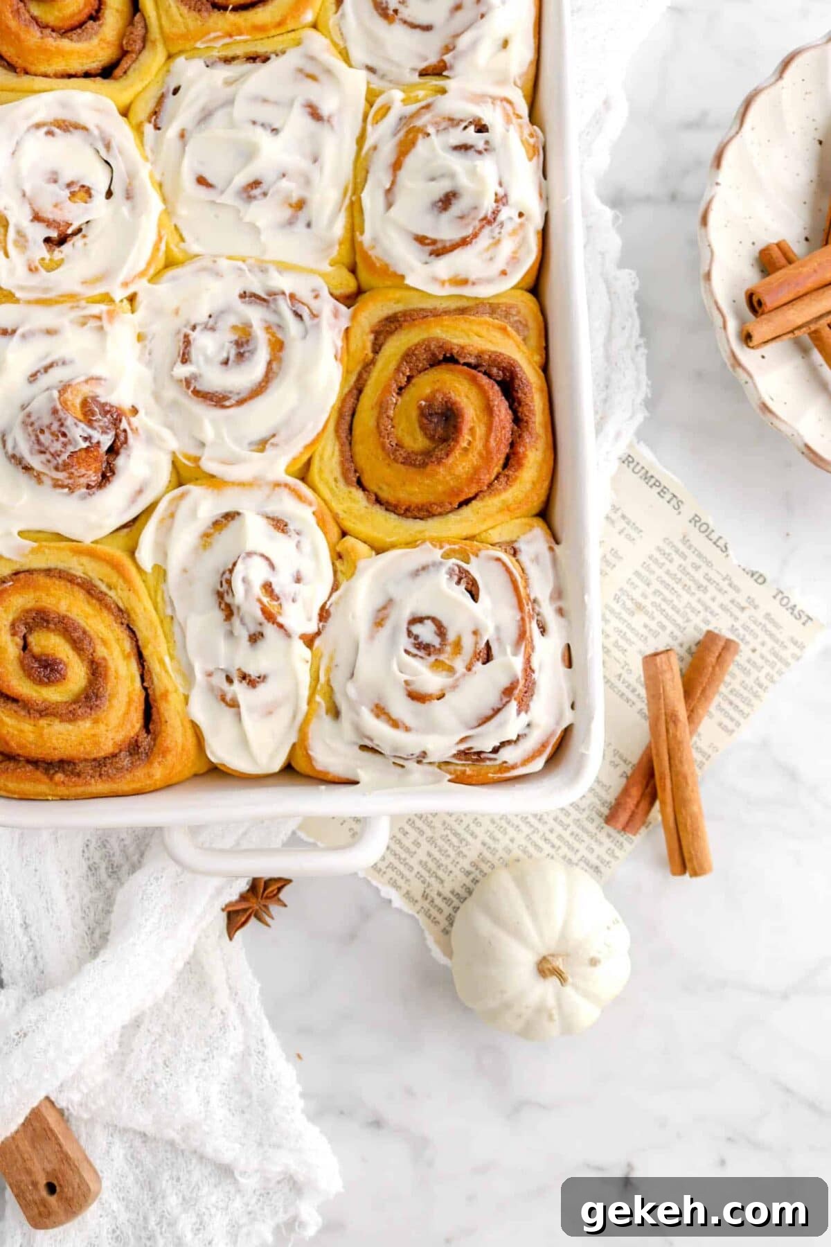 close up of pumpkin cinnamon rolls with mini white pumpkin, cook page, and cinnamon sticks