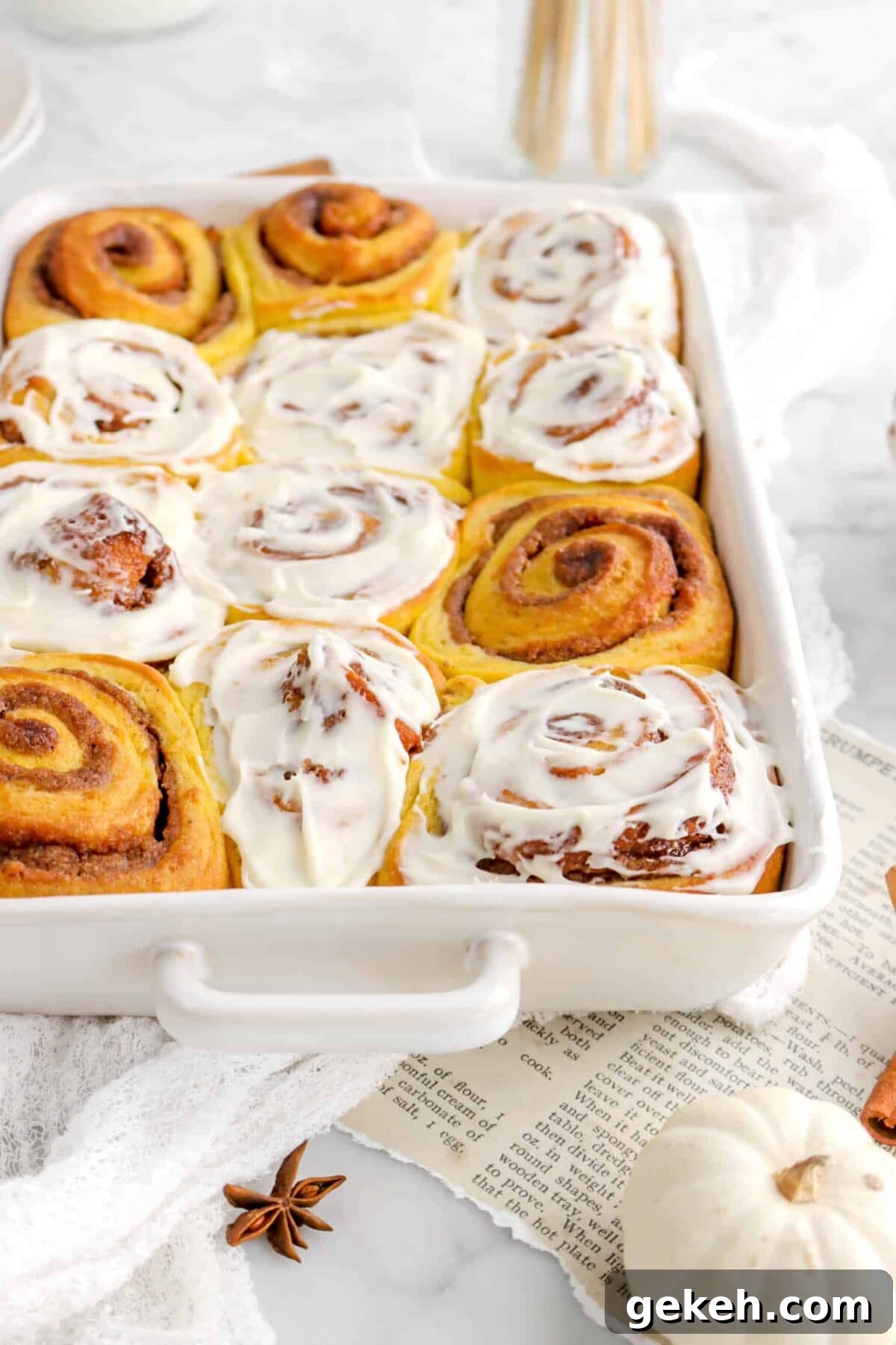 pumpkin cinnamon rolls with some frosted in white casserole dish