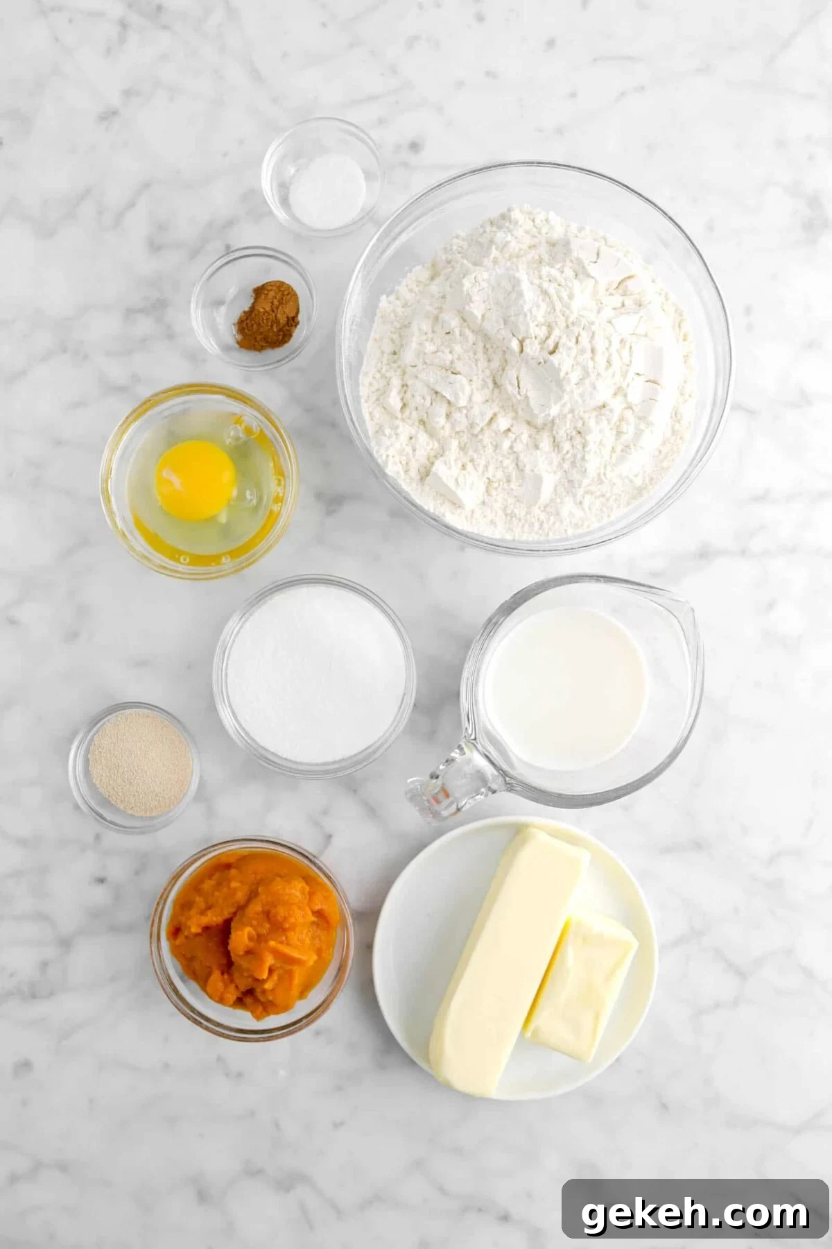 salt, pumpkin pie spice, flour, egg, sugar, milk, butter, pumpkin, and yeast on marble counter