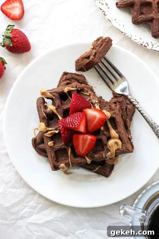 Two Chocolate Whole Wheat Waffles on a plate with strawberries and peanut butter.