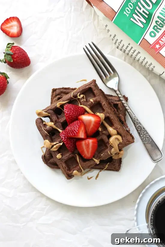 These simple chocolate whole wheat waffles are easy to make and delicious! Light, fluffy and chocolate-y! And made with 100% whole wheat flour! A white plate with two Chocolate Whole Wheat Waffles and a bag of flour and coffee off to the side.