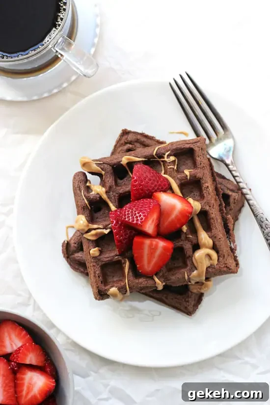 Freezer-friendly chocolate whole wheat waffles! Simple, wholesome and made with 100% whole wheat flour! Make a batch on the weekend for busy mornings! A plate with two Chocolate Whole Wheat Waffles and a bowl of strawberries and coffee off to the side.