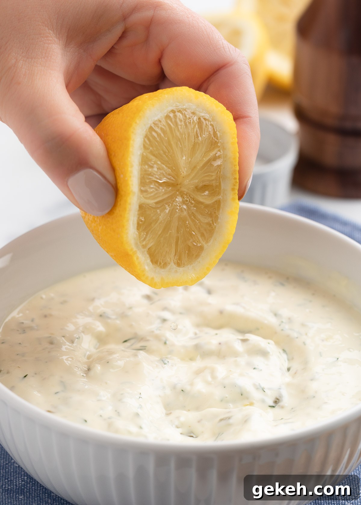 squeezing juice from a halved lemon into a white bowl of tartar sauce