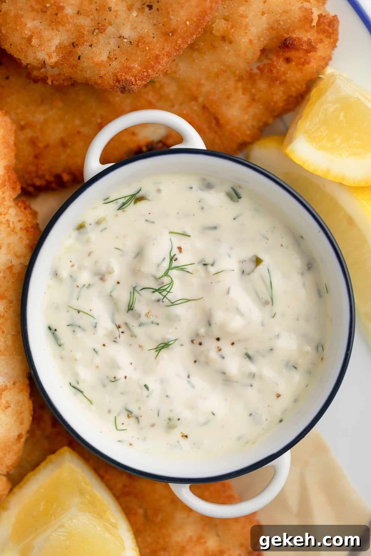 overhead closeup photo of homemade tartar sauce in a white handled bowl on a platter of fried fish