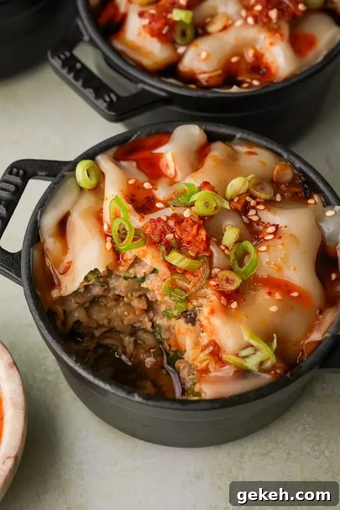 A mini cocotte of dumpling lasagna is shown partially eaten, exposing the layered pork filling beneath the wonton wrappers and garnished with chili oil and scallions.
