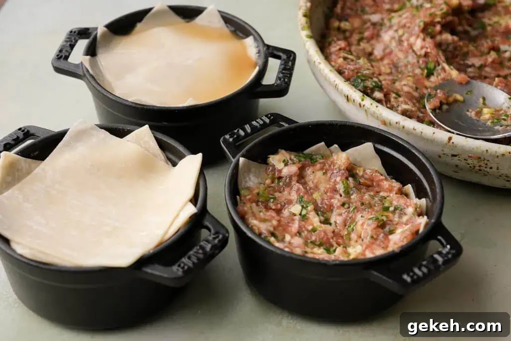 Several mini black cocottes are partially assembled with layers of wonton wrappers and pork filling, with extra wrappers and the remaining meat mixture visible nearby.