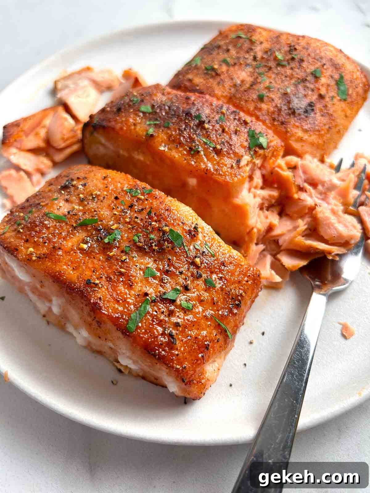 Crispy Air Fryer Salmon Recipe — Quick Flavorful Meal 2 salmon filets on plate with one salmon being flaked apart with a fork.