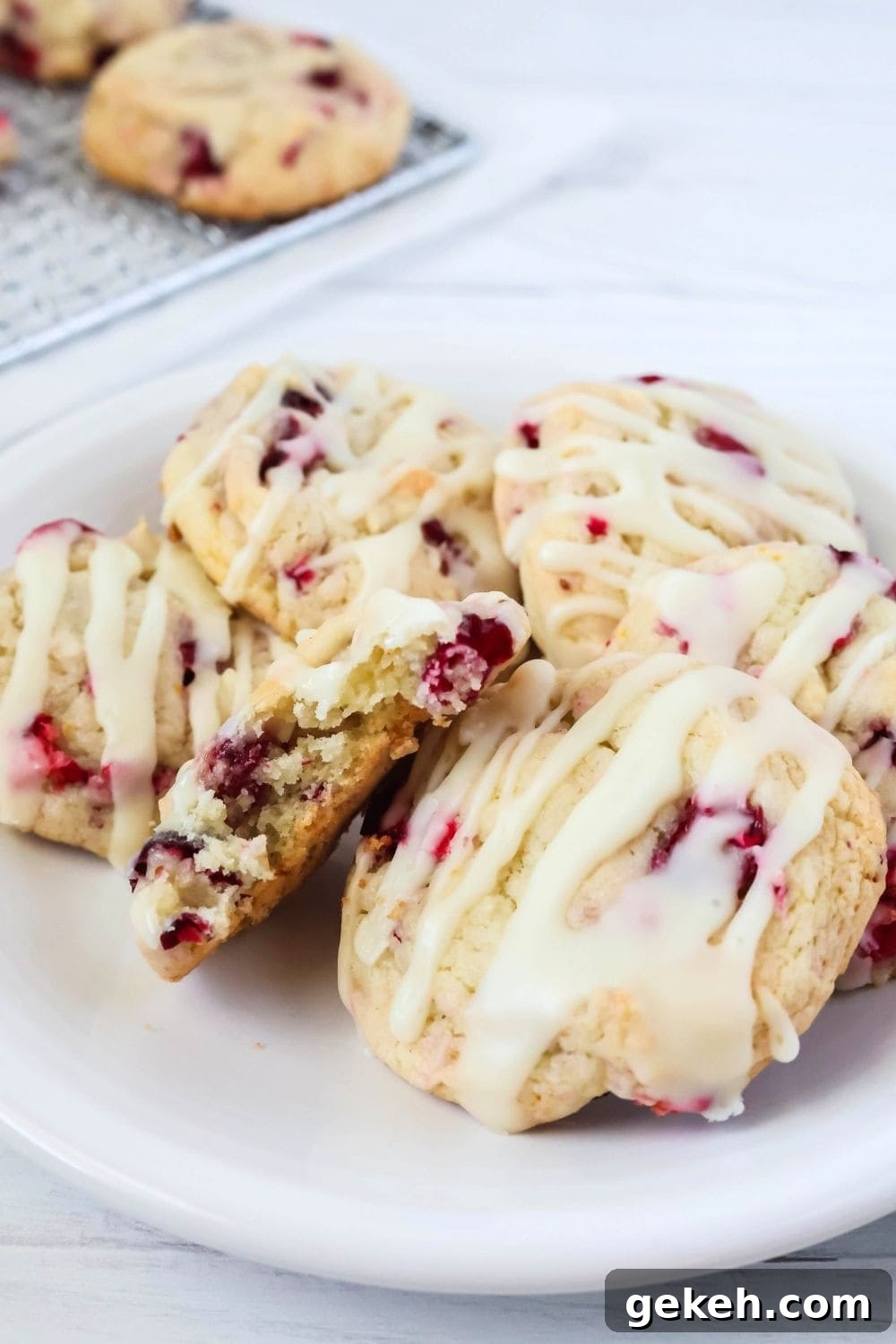 several cranberry orange cookies on a white plate; one cookie has a bite taken out of it, showing its soft and chewy interior.