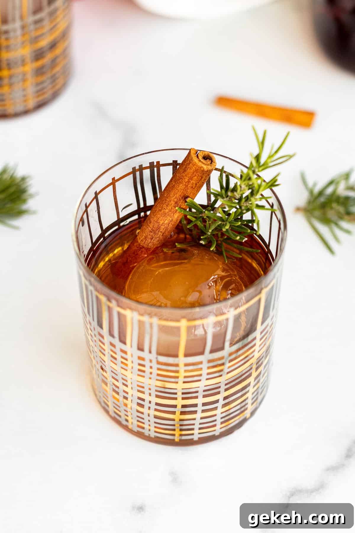 Winter Old-Fashioned Cocktail Recipe: Cozy Seasonal Bourbon Drink 2 cocktail glass with a clear ice ball and winter old fashioned garnished with rosemary and cinnamon stick sitting on marble counter