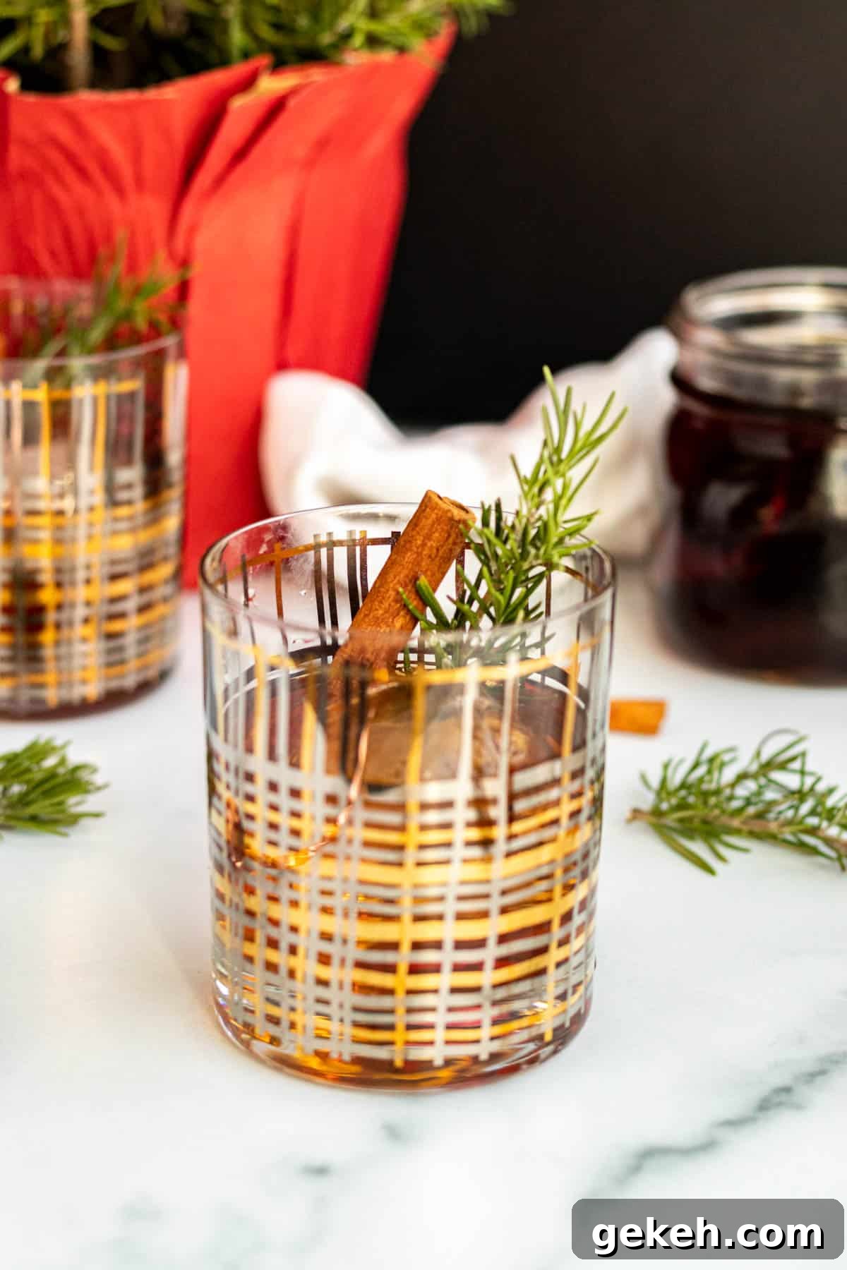 Winter Old-Fashioned Cocktail Recipe: Cozy Seasonal Bourbon Drink 4 winter old fashioned cocktail in a gold and silver striped rocks glass with rosemary sprigs scattered around