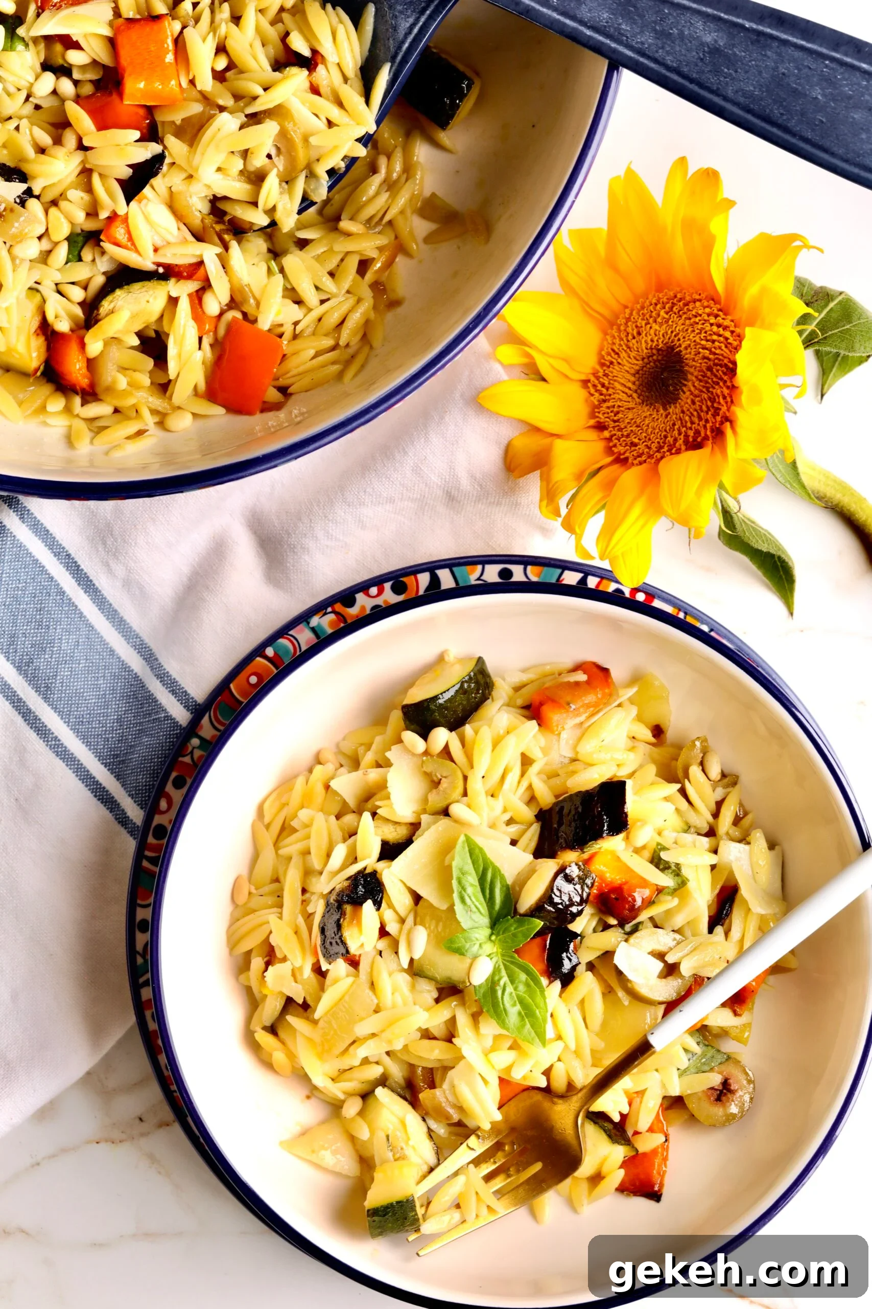 Roasted Vegetable and Parmesan Orzo Recipe 2 Fork in a bowl of orzo past with roasted vegetables and parmesan next to a sunflower.