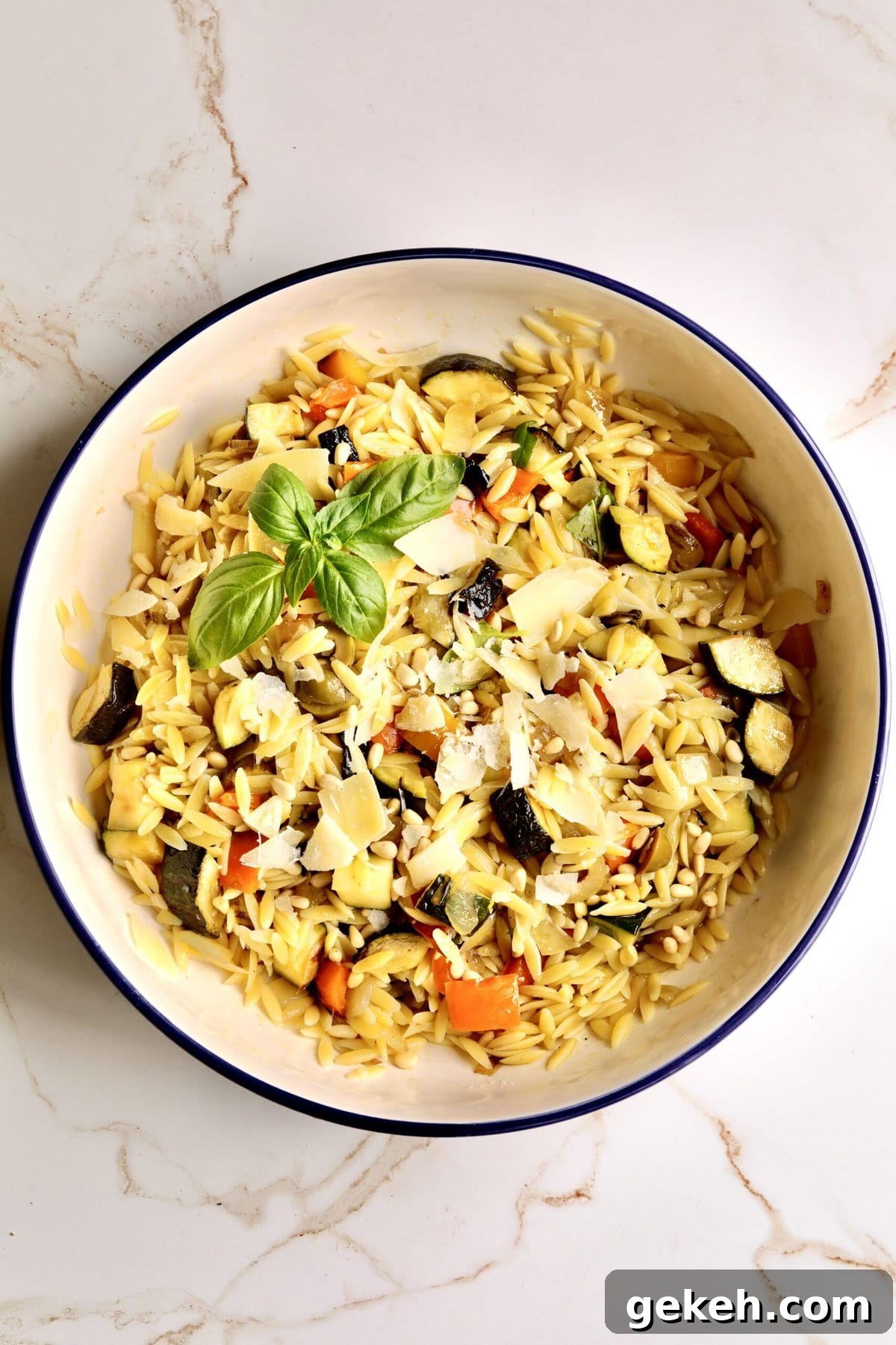 Roasted Vegetable and Parmesan Orzo Recipe 10 easy orzo pasta with roasted veggies in a large serving bowl. Thick slices of Parmesan cheese on top. Basil to garish.