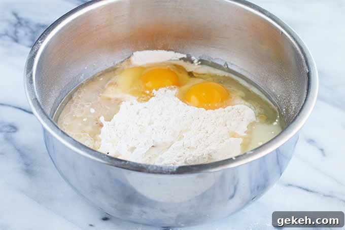 Classic Old-Fashioned Crumb Cake Recipe: Timeless Coffee Cake Delight 10 A stainless steel mixing bowl filled with flour, two eggs, and other ingredients to make a cake batter, on a gray and white marble surface.
