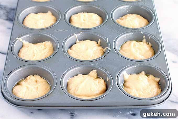 Classic Old-Fashioned Crumb Cake Recipe: Timeless Coffee Cake Delight 11 A metal muffin tin with nine wells filled two-thirds of the way with a thick beige batter, on a gray and white marble background.