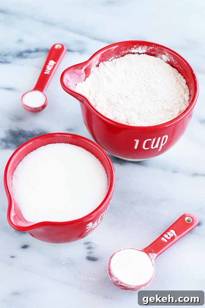Classic Old-Fashioned Crumb Cake Recipe: Timeless Coffee Cake Delight 8 Red measuring cups with spouts filled with flour and sugar alongside red plastic measuring spoons of baking powder and salt, on a gray and white marble background.