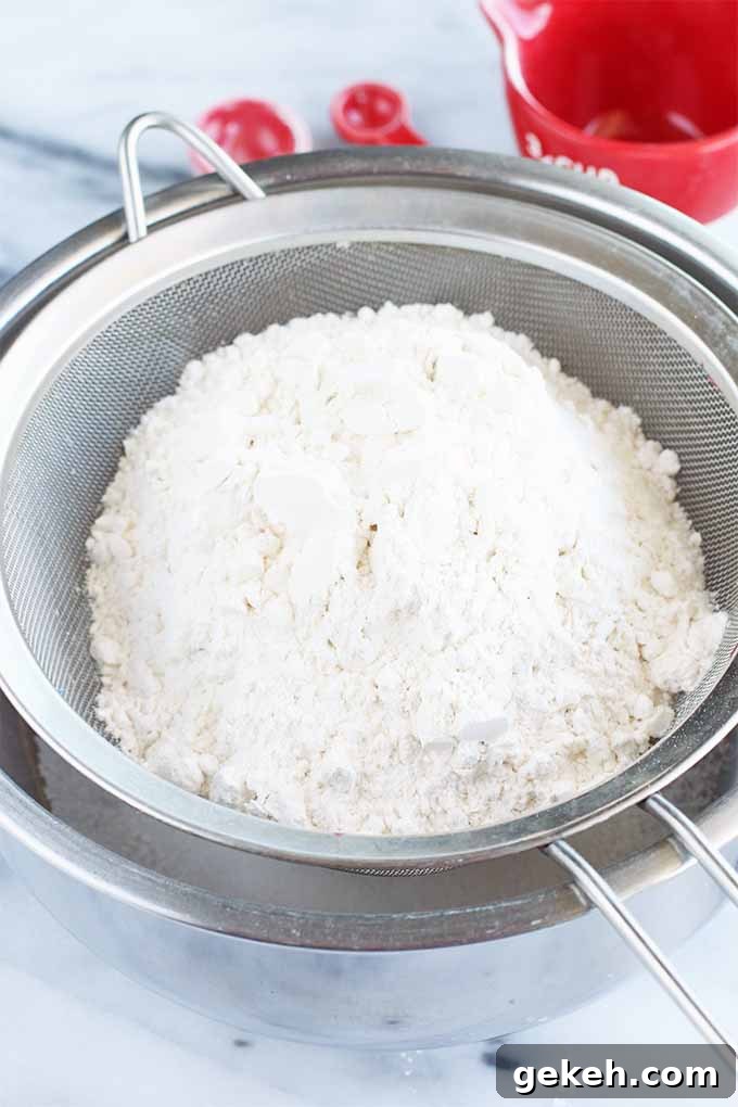 Classic Old-Fashioned Crumb Cake Recipe: Timeless Coffee Cake Delight 9 A fine mesh sieve full of flour rests in a stainless steel mixing bowl, on a marble surface.