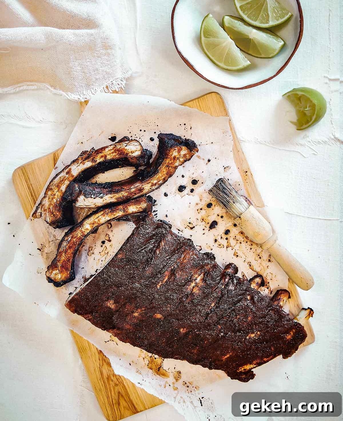 Vietnamese-Style Caramelized Pork Ribs with Garlic and Fish Sauce 2 A rack of Vietnamese pork ribs on a sheet of parchment on a cutting board with a basting brush and a bowl of lime wedges nearby.