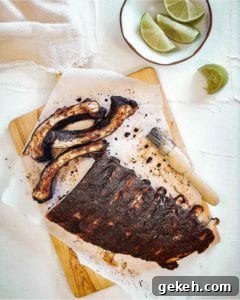 Vietnamese-Style Caramelized Pork Ribs with Garlic and Fish Sauce 3 A rack of Vietnamese pork ribs on a sheet of parchment on a cutting board with a basting brush and a bowl of lime wedges nearby.