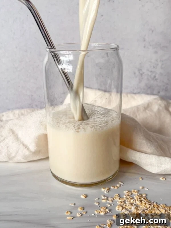 Creamy Homemade Oat Milk Recipe — Simple Step-by-Step Guide 3 A glass of oat milk is being poured, with a metal straw inside.
