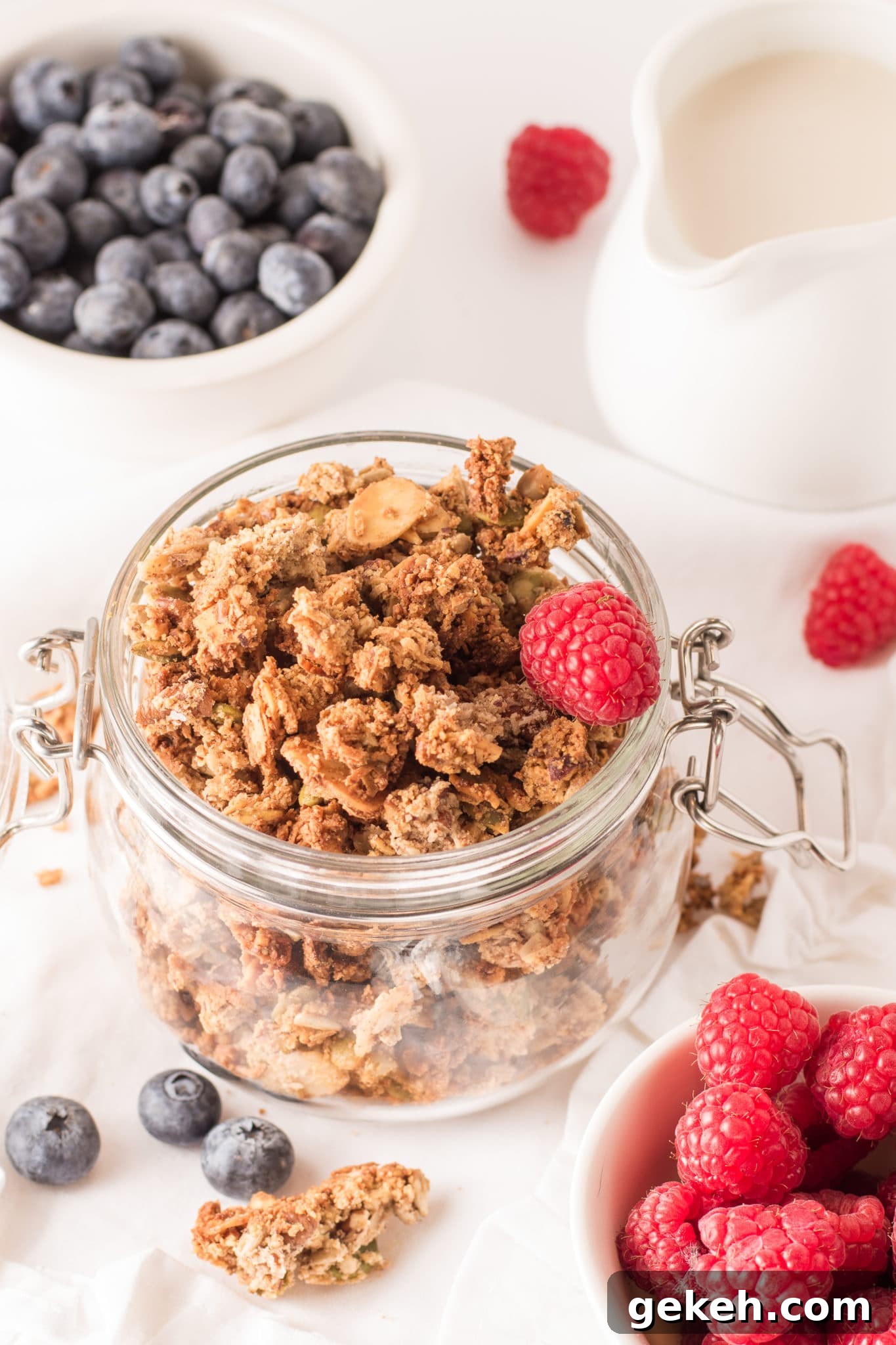 Maple Spice Low-Carb Granola — Crispy, Chewy, Gluten-Free Keto 6 A glass mason jar filled with low carb granola cluster surrounded by bowls of fresh blueberries and raspberries.