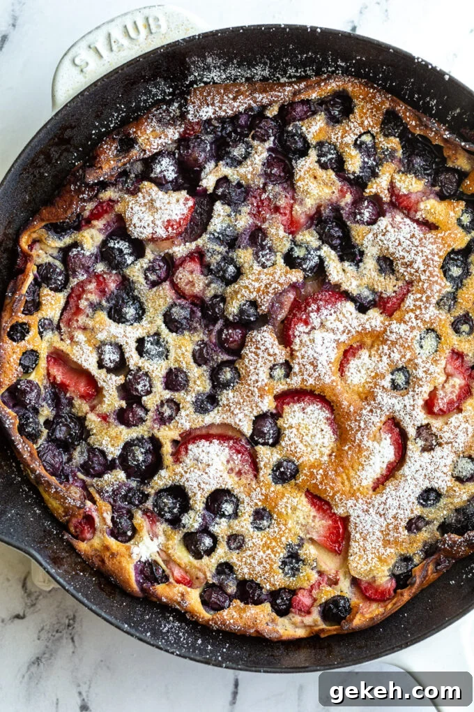 Berry Dutch Baby Pancake: Fluffy Skillet Dessert with Fresh Berries 2 blueberry and strawberry dutch baby in a white skillet and dusted with powdered sugar