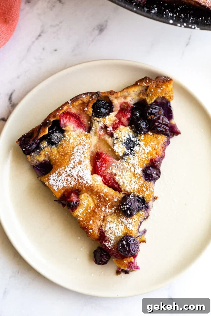 Berry Dutch Baby Pancake: Fluffy Skillet Dessert with Fresh Berries 3 slice of blueberry and strawberry dutch baby dusted with powdered sugar