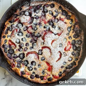 Berry Dutch Baby Pancake: Fluffy Skillet Dessert with Fresh Berries 5 blueberry and strawberry dutch baby in a white skillet and dusted with powdered sugar
