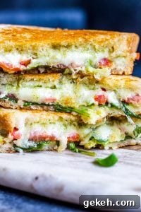 Grilled Goat Cheese Sandwich with pesto, mozzarella, tomatoes, arugula and avocado. Close up straight on shot of grilled cheese cut in half and piled on top of each other.
