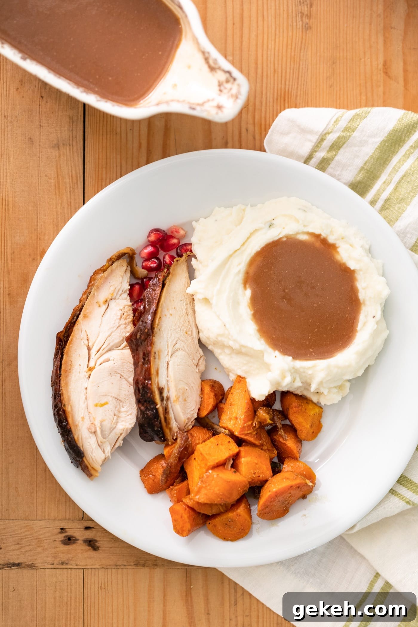Homemade Gravy Recipe: Smooth, Rich Sauce in Minutes 5 Top down view of plate filled with Thanksgiving dishes including white mashed potatoes topped with homemade gravy with extra gravy in white container to the side all on wood surface