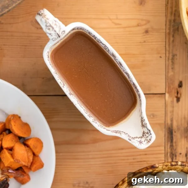 Homemade Gravy Recipe: Smooth, Rich Sauce in Minutes 6 Top down view of brown colored homemade gravy in a white gravy container with extra food sitting on white plate and extra side dishes around all on wood surface
