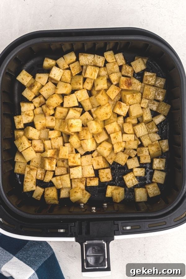 Crispy Air Fryer Breakfast Potatoes Recipe 4 Soaked and seasoned cubes of potatoes, in an air fryer basket. Uncooked.