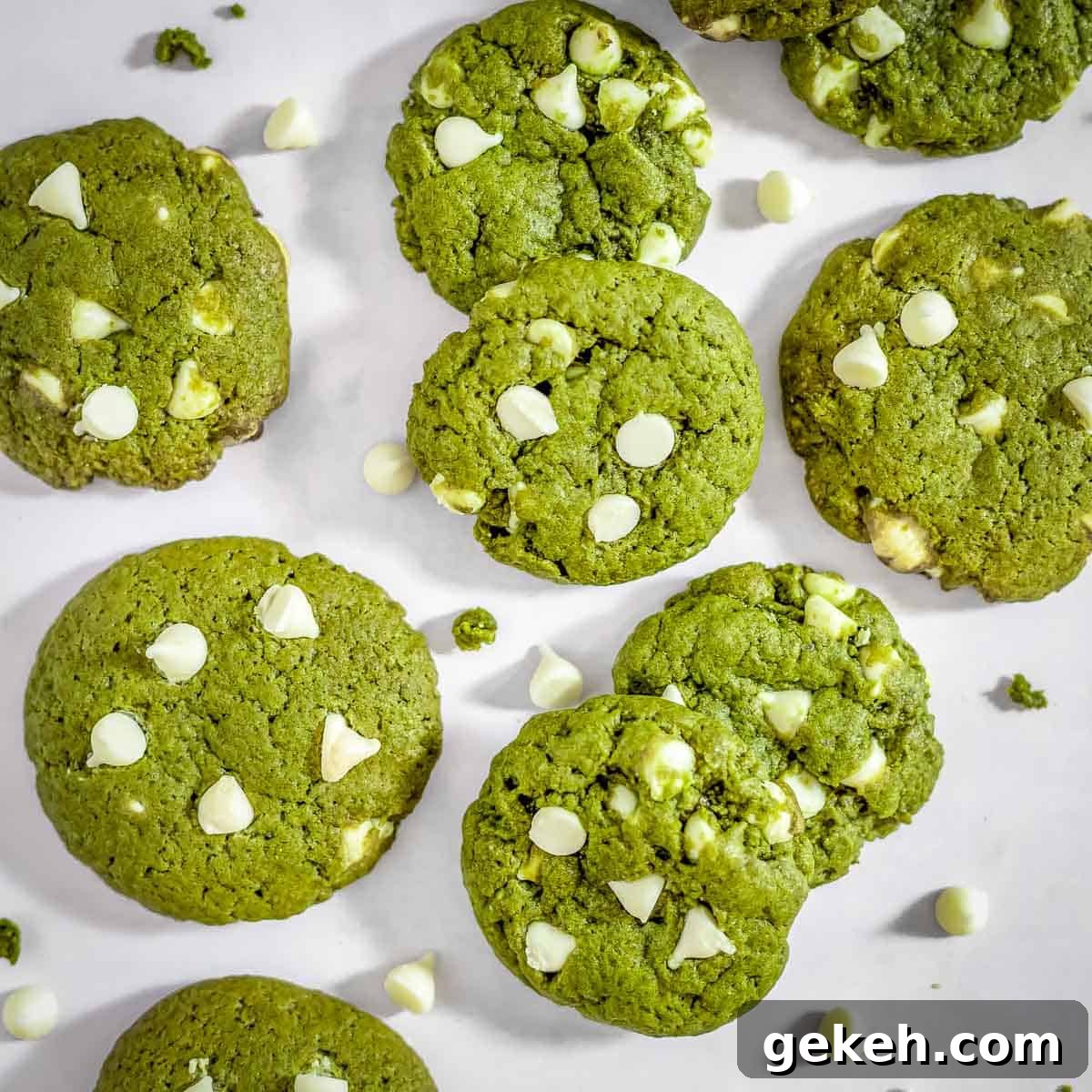 Overhead shot of many matcha cookies scattered on parchment paper with white chocolate chips sprinkled around.