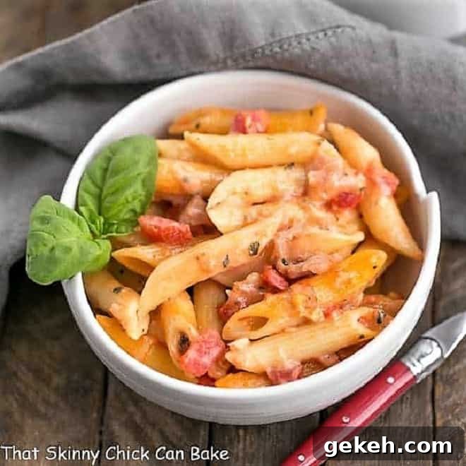 Cheesy Baked Pasta - Creamy pasta with 3 cheeses, basil and prosciutto Overhead view of Cheesy Baked Pasta in a white bowl with a sprig of basil