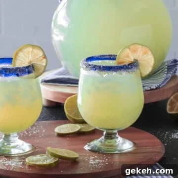 Margarita glasses with lime wedges next to a pitcher.