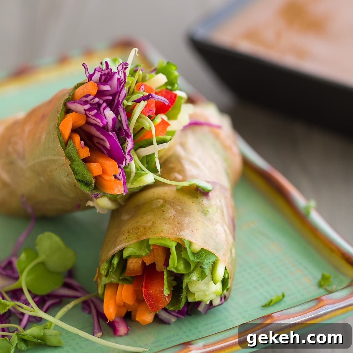 Colorful vegetable summer rolls with a rainbow of colors in brown rice paper on a light green plate.
