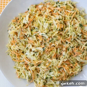 White shallow bowl stilled with green cabbage coleslaw, carrots, and parsley with a light dressing.