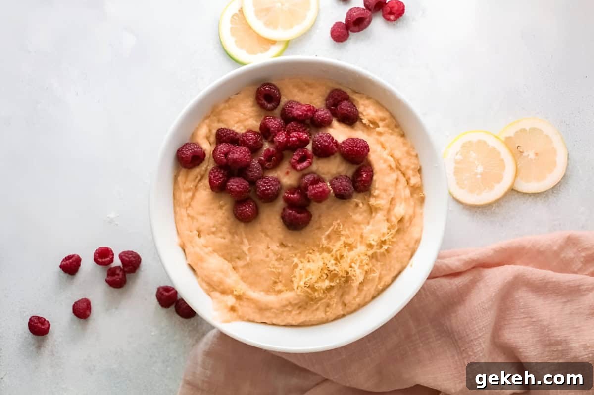 adding lemon zest and raspberries to olive oil cake batter in a white bowl.